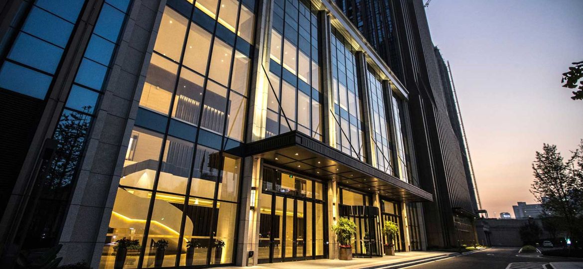 Front entrance to an office building with a glass facade and lit from within.