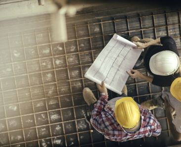 Architect, foreman and engineer on a construction site, looking down on a blueprint.