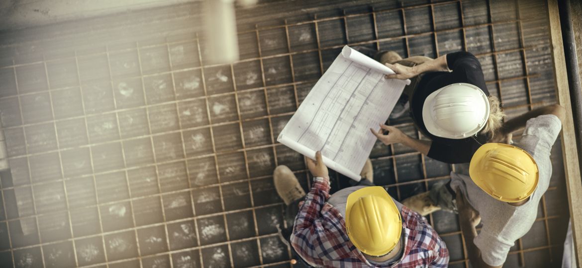 Architect, foreman and engineer on a construction site, looking down on a blueprint.